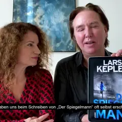 Ein Mann und eine Frau präsentieren ein Tablet mit dem Cover von "Der Spiegelmann" von Lars Kepler.