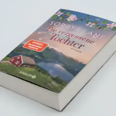 Ein Buchcover mit dem Titel "Die vergessene Tochter" von Soraya Lane. Es zeigt eine rote Hütte am See vor einer Bergkulisse.
