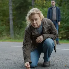Eine Frau kniet auf einer Straße und untersucht etwas am Boden. Im Hintergrund steht ein Mann. Typische Szene für spannende Krimis aus dem Norden.