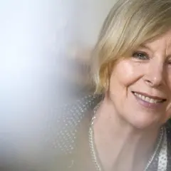 Porträt von Dagmar Ploetz, die lächelnd in die Kamera blickt. Sie trägt eine silberne Kette und ein gemustertes Oberteil.