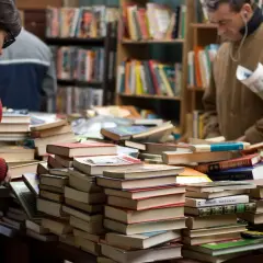 Stapel von Büchern in einem Antiquariat. Eine Frau und ein Mann suchen nach historischen Romanen, die auf wahren Begebenheiten basieren.