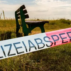 Polizeisperrband vor einer grünen Parkbank in einer Wiese. Ein Tatort, der Stoff für die besten Regionalkrimis liefert.