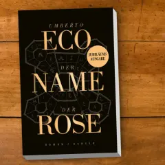 Umberto Ecos Roman "Im Namen der Rose" als Jubiläumsausgabe auf Holztisch.