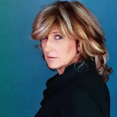Jilliane Hoffman, mit ihrem charakteristischen blonden Haar und einem nachdenklichen Blick, posiert vor einem blauen Hintergrund.