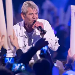 Ein Sänger singt auf der Bühne, umgeben von Fans mit Lichtern. Er scheint zu sagen: "Wie lieb ich dich hab", und die Menge jubelt.