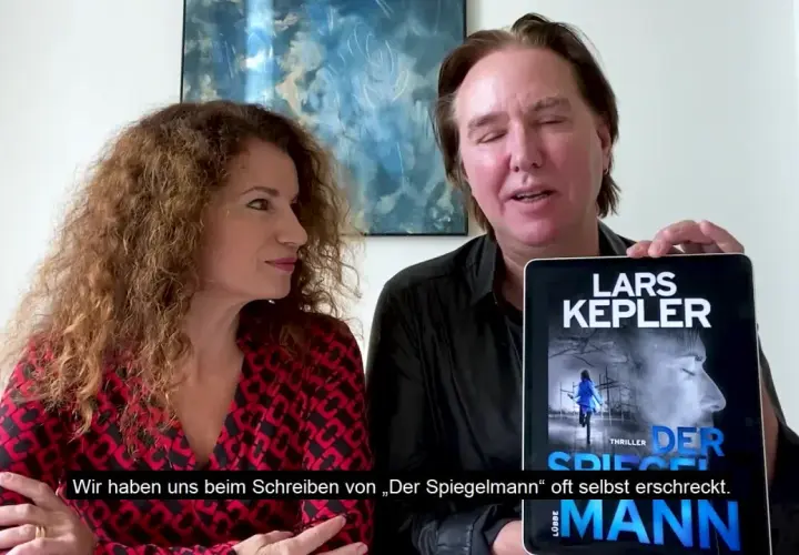 Ein Mann und eine Frau präsentieren ein Tablet mit dem Cover von "Der Spiegelmann" von Lars Kepler.