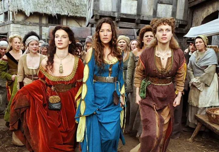 Drei Frauen in historischen Gewändern, die an eine "die wanderhure reihenfolge" erinnern, gehen durch eine mittelalterliche Gasse.