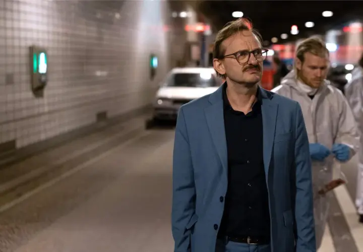 Ein Mann im blauen Anzug, vielleicht ein Ermittler wie Danowski, steht im Tunnel. Im Hintergrund arbeiten Personen in Schutzanzügen.