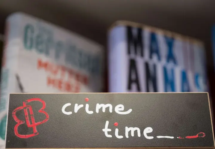 Ein Schild mit der Aufschrift "crime time" und einem roten Logo. Im Hintergrund unscharfe Bücher, die auf gemütliche Krimi-Lektüre hindeuten.
