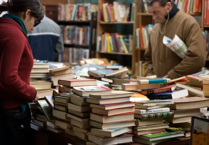 Stapel von Büchern in einem Antiquariat. Eine Frau und ein Mann suchen nach historischen Romanen, die auf wahren Begebenheiten basieren.