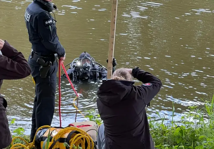 Polizei-Taucher sucht nach Beweisen. Ein Polizist sichert die Leine, während eine Frau die Tiefe misst. Ein Fall von mord auf hoher see?