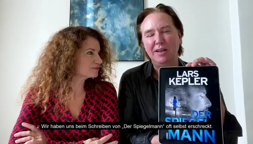 Ein Mann und eine Frau präsentieren ein Tablet mit dem Cover von "Der Spiegelmann" von Lars Kepler.