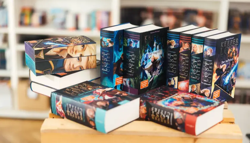 Stapel von "Keeper of the Lost Cities" Büchern, eine beliebte Fantasy-Buchreihe für Erwachsene, mit farbenfrohen Covern und Illustrationen.