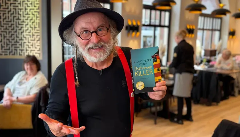 Klaus-Peter Wolf präsentiert "Ostfriesenkiller", Band 1 seiner Krimireihe. Ein Mann mit Hut und roten Hosenträgern hält das Buch hoch.