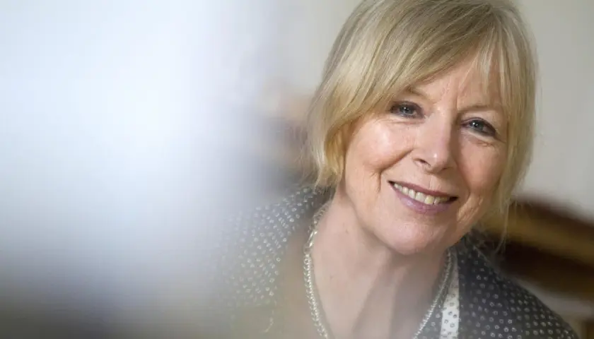 Porträt von Dagmar Ploetz, die lächelnd in die Kamera blickt. Sie trägt eine silberne Kette und ein gemustertes Oberteil.