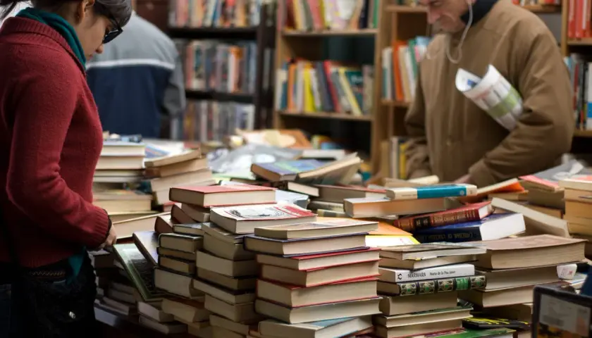 Stapel von Büchern in einem Antiquariat. Eine Frau und ein Mann suchen nach historischen Romanen, die auf wahren Begebenheiten basieren.