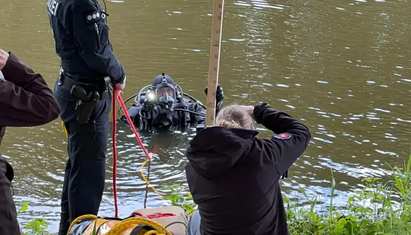 Polizei-Taucher sucht nach Beweisen. Ein Polizist sichert die Leine, während eine Frau die Tiefe misst. Ein Fall von mord auf hoher see?
