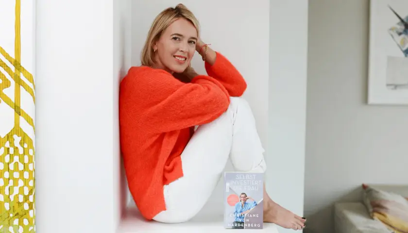 Christiane von Hardenberg sitzt lächelnd mit einem Buch in der Hand.