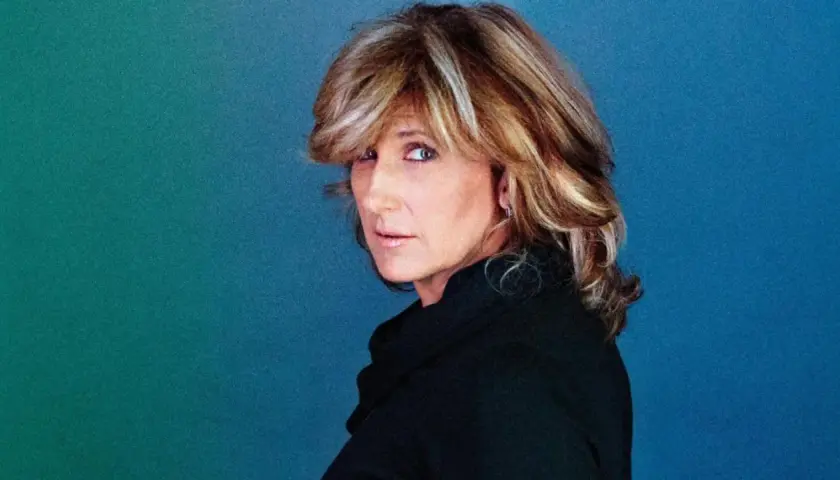Jilliane Hoffman, mit ihrem charakteristischen blonden Haar und einem nachdenklichen Blick, posiert vor einem blauen Hintergrund.