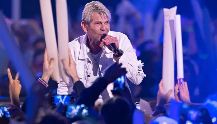 Ein Sänger singt auf der Bühne, umgeben von Fans mit Lichtern. Er scheint zu sagen: "Wie lieb ich dich hab", und die Menge jubelt.