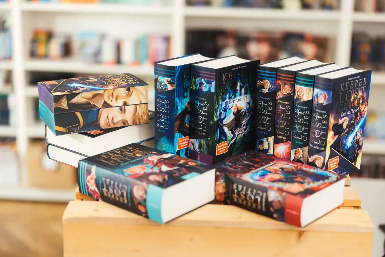 Stapel von "Keeper of the Lost Cities" Büchern, eine beliebte Fantasy-Buchreihe für Erwachsene, mit farbenfrohen Covern und Illustrationen.
