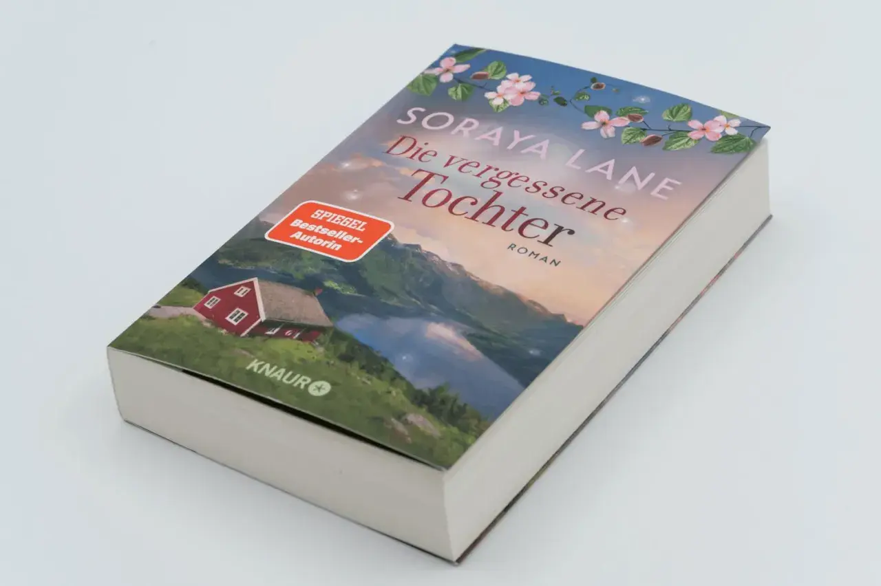 Ein Buchcover mit dem Titel "Die vergessene Tochter" von Soraya Lane. Es zeigt eine rote Hütte am See vor einer Bergkulisse.