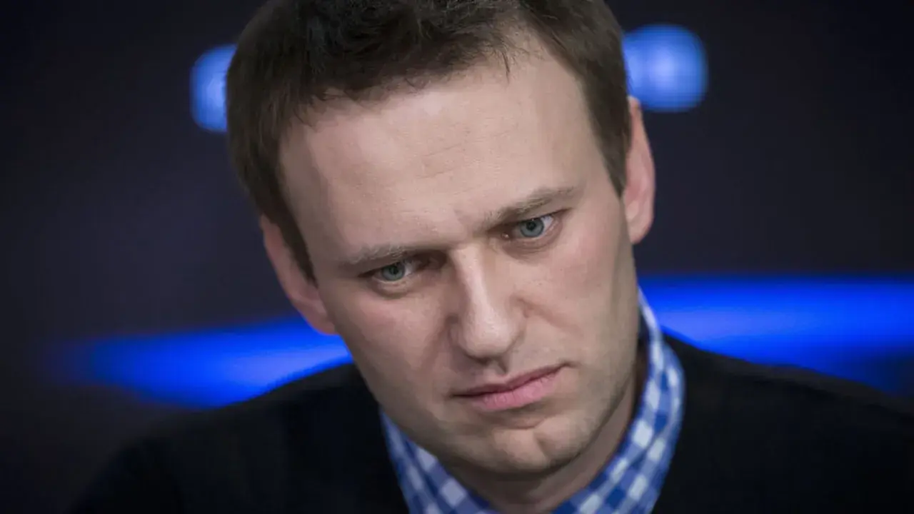 Alexei Nawalny, mit ernstem Blick und blau kariertem Hemd, im Scheinwerferlicht.