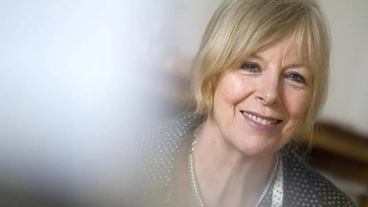 Porträt von Dagmar Ploetz, die lächelnd in die Kamera blickt. Sie trägt eine silberne Kette und ein gemustertes Oberteil.
