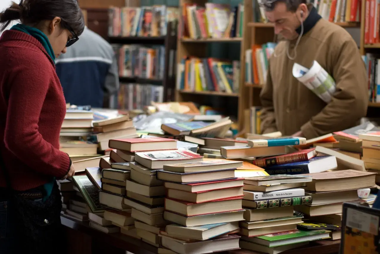 Stapel von Büchern in einem Antiquariat. Eine Frau und ein Mann suchen nach historischen Romanen, die auf wahren Begebenheiten basieren.