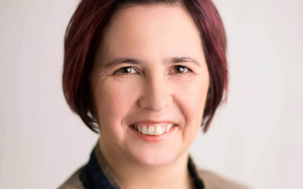 Nicole Peters lächelt freundlich in die Kamera. Ihr kurz geschnittenes, dunkelrotes Haar umrahmt ihr Gesicht.