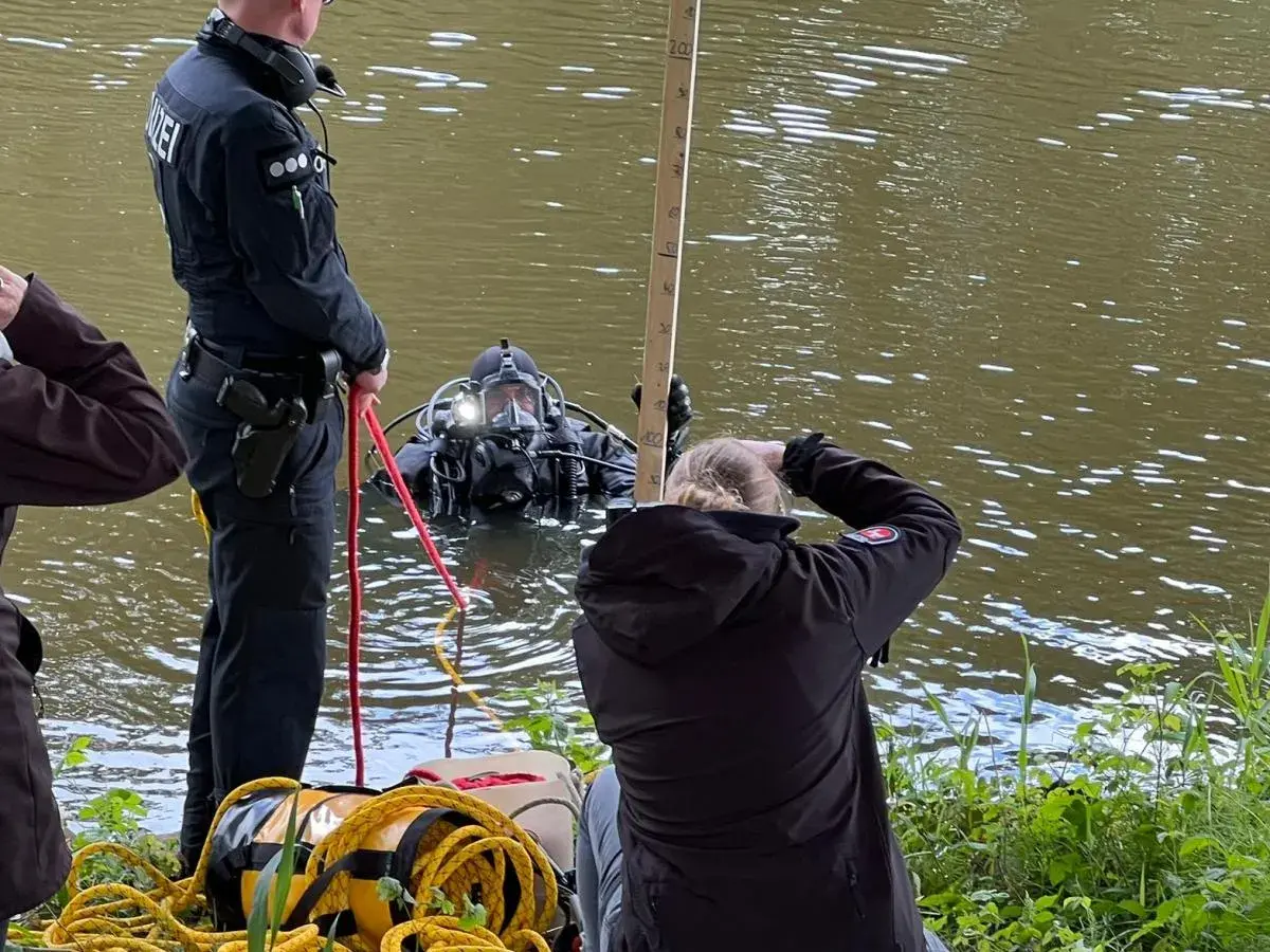 Polizei-Taucher sucht nach Beweisen. Ein Polizist sichert die Leine, während eine Frau die Tiefe misst. Ein Fall von mord auf hoher see?