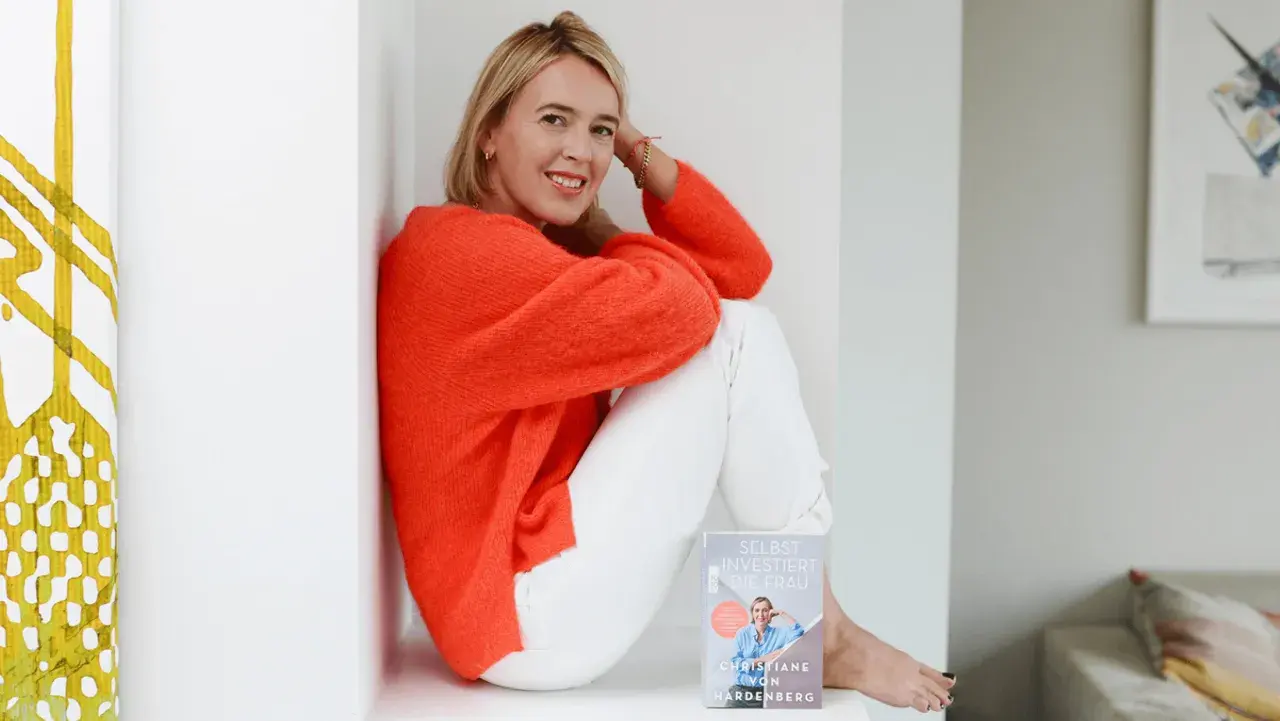 Christiane von Hardenberg sitzt lächelnd mit einem Buch in der Hand.