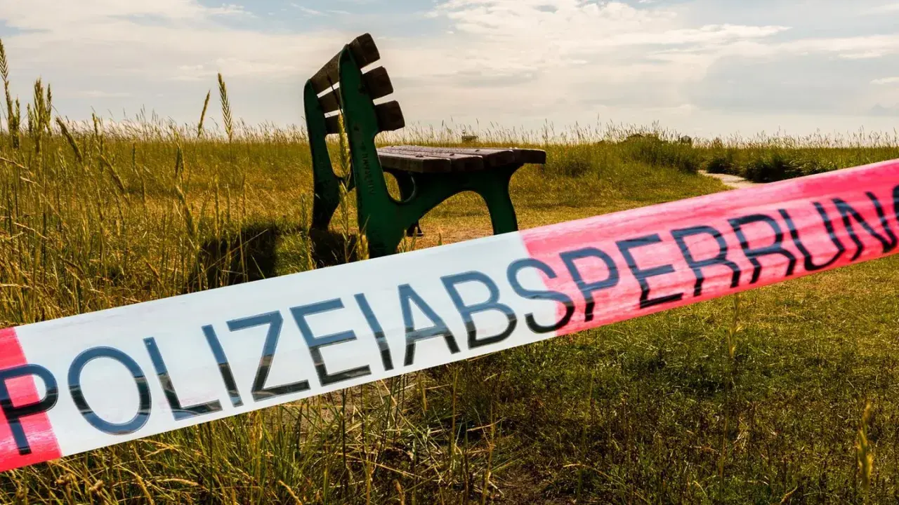 Polizeisperrband vor einer grünen Parkbank in einer Wiese. Ein Tatort, der Stoff für die besten Regionalkrimis liefert.