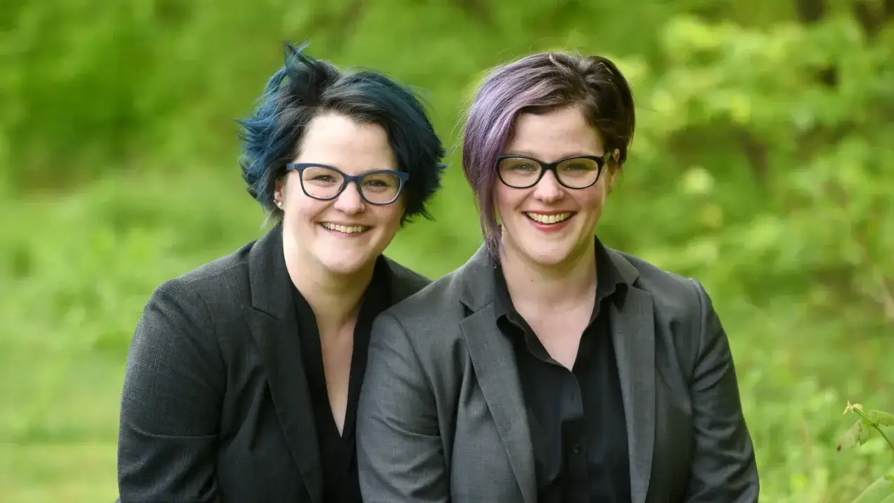 Emily Nagoski und ihre Schwester lächeln in die Kamera, beide tragen Brillen und Sakkos.