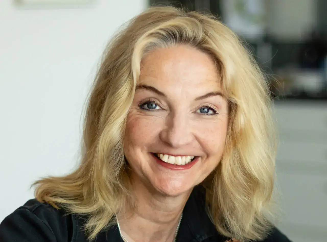 Lächelnde Katja Reider mit blonden Haaren und blauen Augen, trägt ein schwarzes Oberteil.