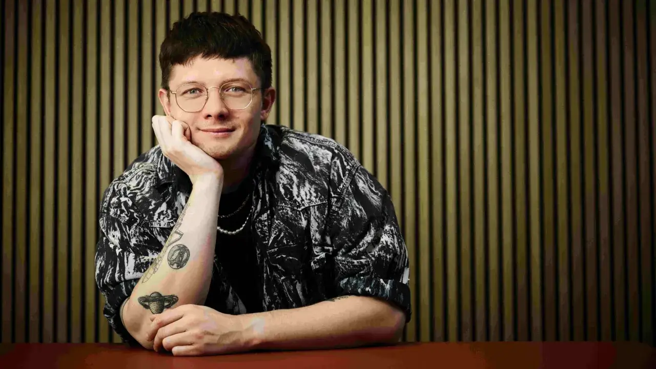 Fritz Espenlaub mit Brille und Tattoos lehnt nachdenklich am Tisch.
